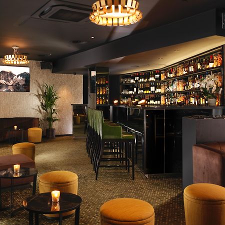 Hotel St Martins Lane Londra Esterno foto The photo depicts a stylish bar or lounge interior. The space features a dark, sophisticated color scheme with plush seating, including brown couches and vibrant yellow stools. A illuminated bar area is prominently displayed, lined with various bottl