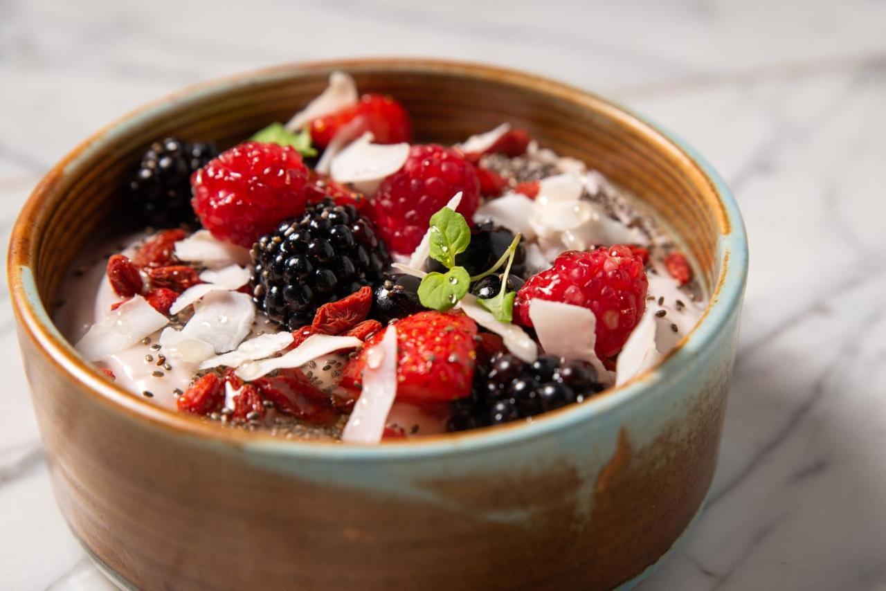 Hotel St Martins Lane Londra Esterno foto The photo shows a bowl of yogurt topped with various fresh fruits and toppings. The toppings include vibrant red raspberries, blackberries, and pieces of dried fruits, along with shredded coconut. There are also some small seeds, possibly chia seeds,