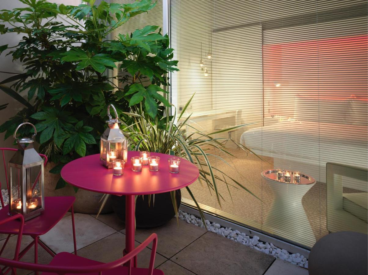 Hotel St Martins Lane Londra Esterno foto The photo depicts a cozy outdoor space with a round pink table and two matching chairs. On the table, there are several lanterns with candles inside, providing a warm ambiance. Surrounding the area are lush green plants, adding a natural touch. In th