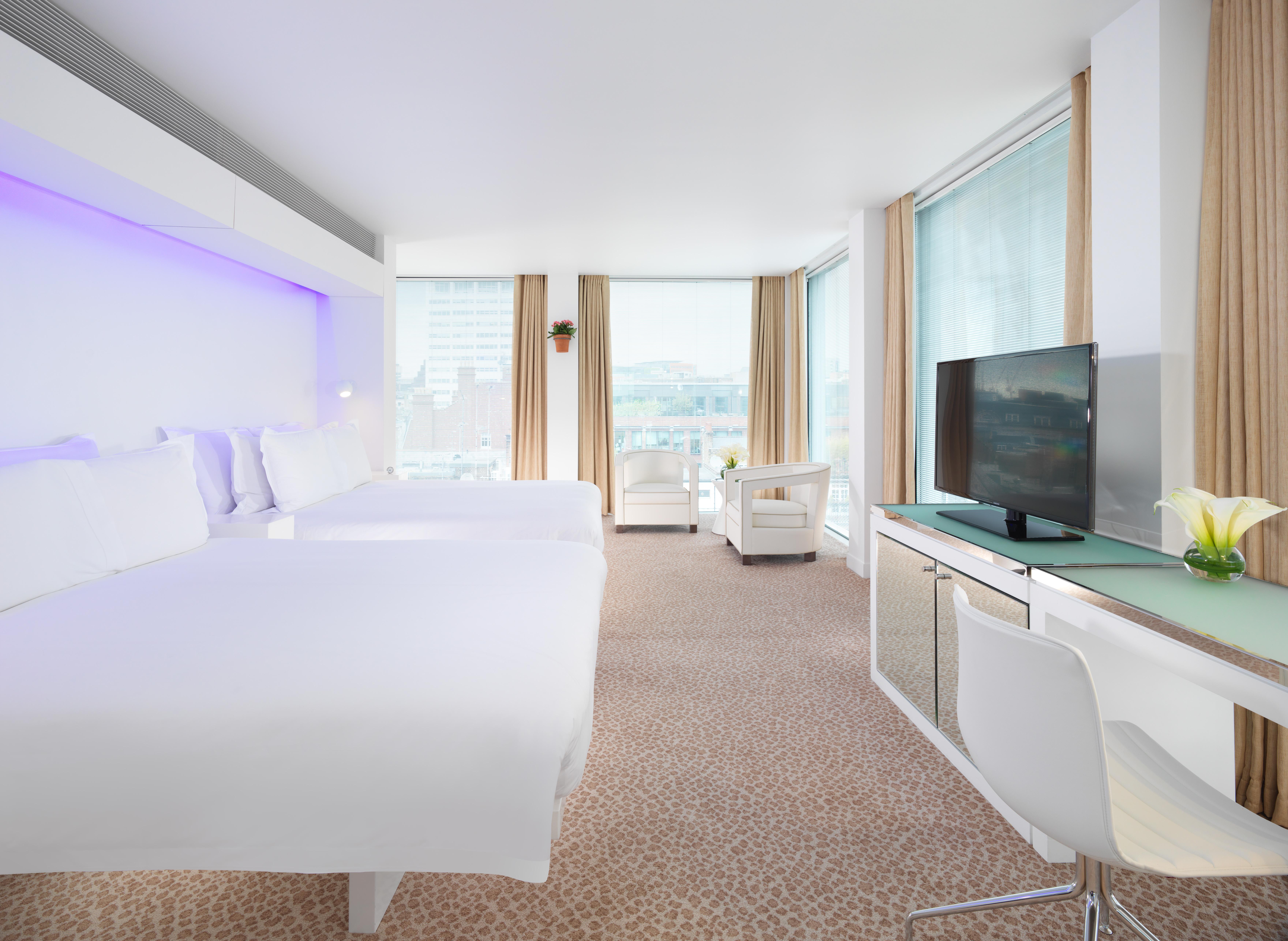 Hotel St Martins Lane Londra Esterno foto The photo shows a modern hotel room featuring two beds with white linens, a sleek design, and large windows allowing natural light to enter. The room includes a comfortable chair, a desk with a television mounted on the wall, and a stylish decorative
