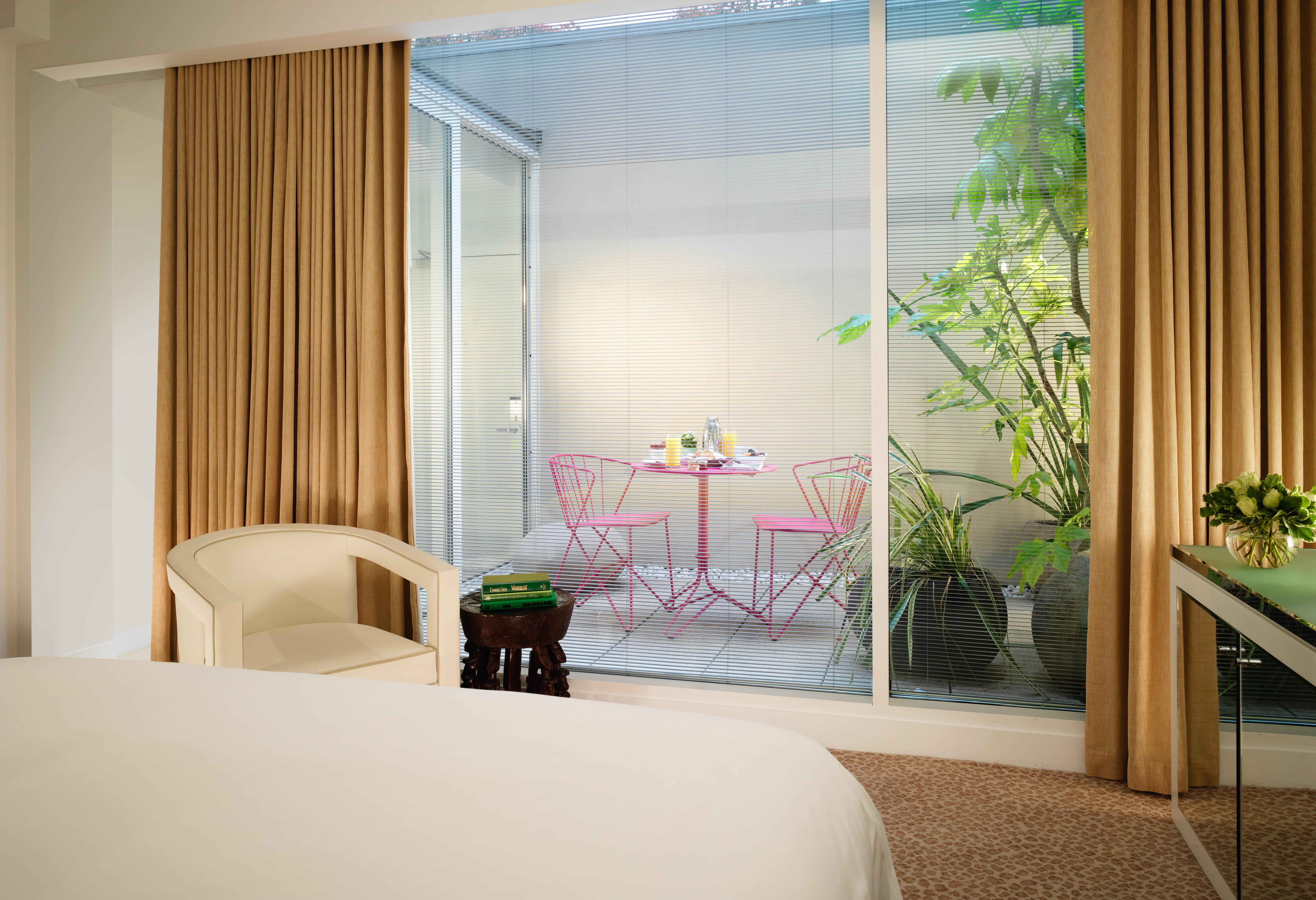 Hotel St Martins Lane Londra Esterno foto The photo depicts a modern room with a bed visible in the foreground. Large glass windows allow natural light to enter, showcasing a small outdoor space. Beyond the glass, there is a charming patio area featuring a round table and two pink chairs, su