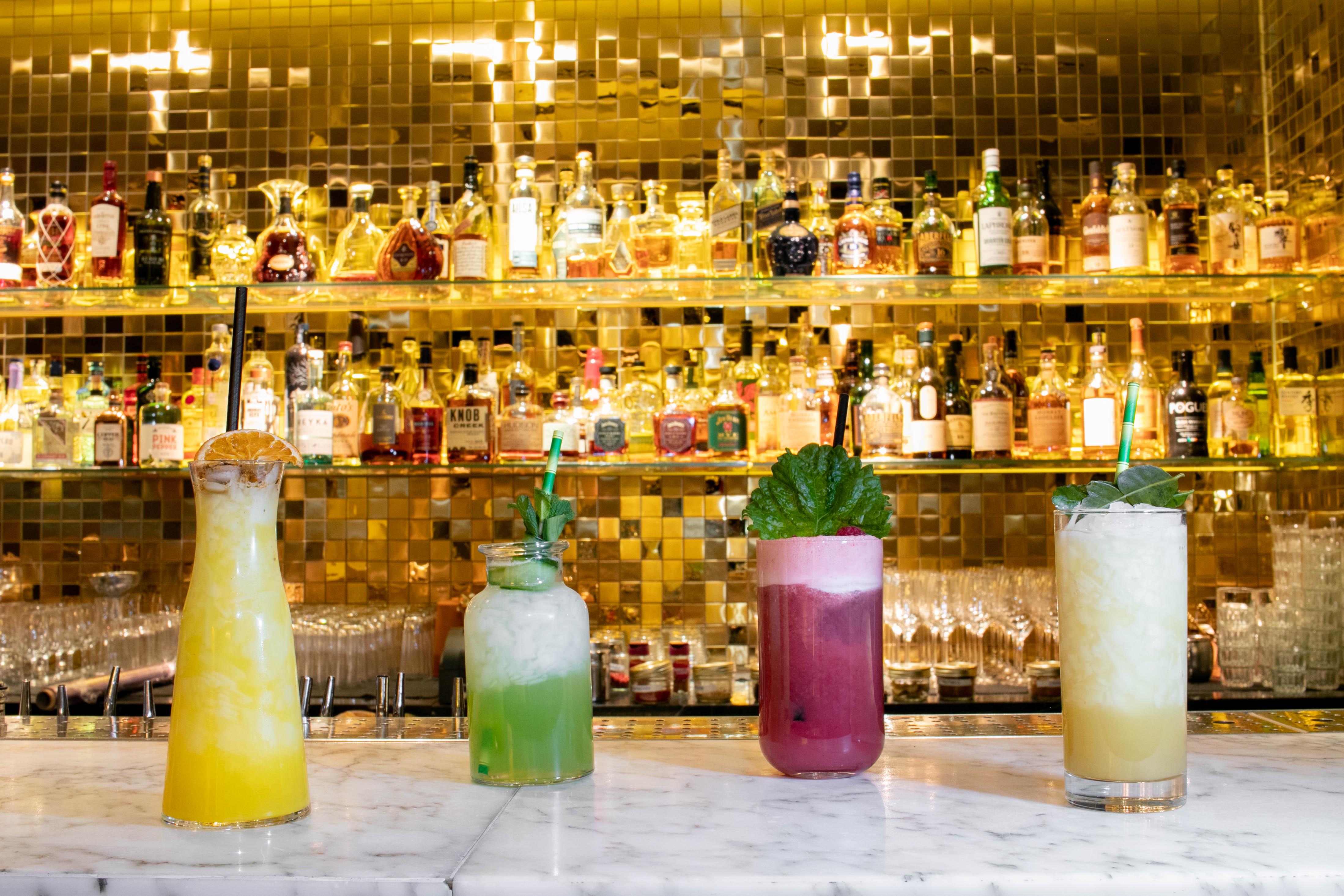 Hotel St Martins Lane Londra Esterno foto The photo features a stylish bar scene with four colorful cocktails displayed on a marble countertop. Behind the drinks, there is a sparkling, gold mosaic wall lined with various liquor bottles, creating an upscale ambiance. The cocktails include vib