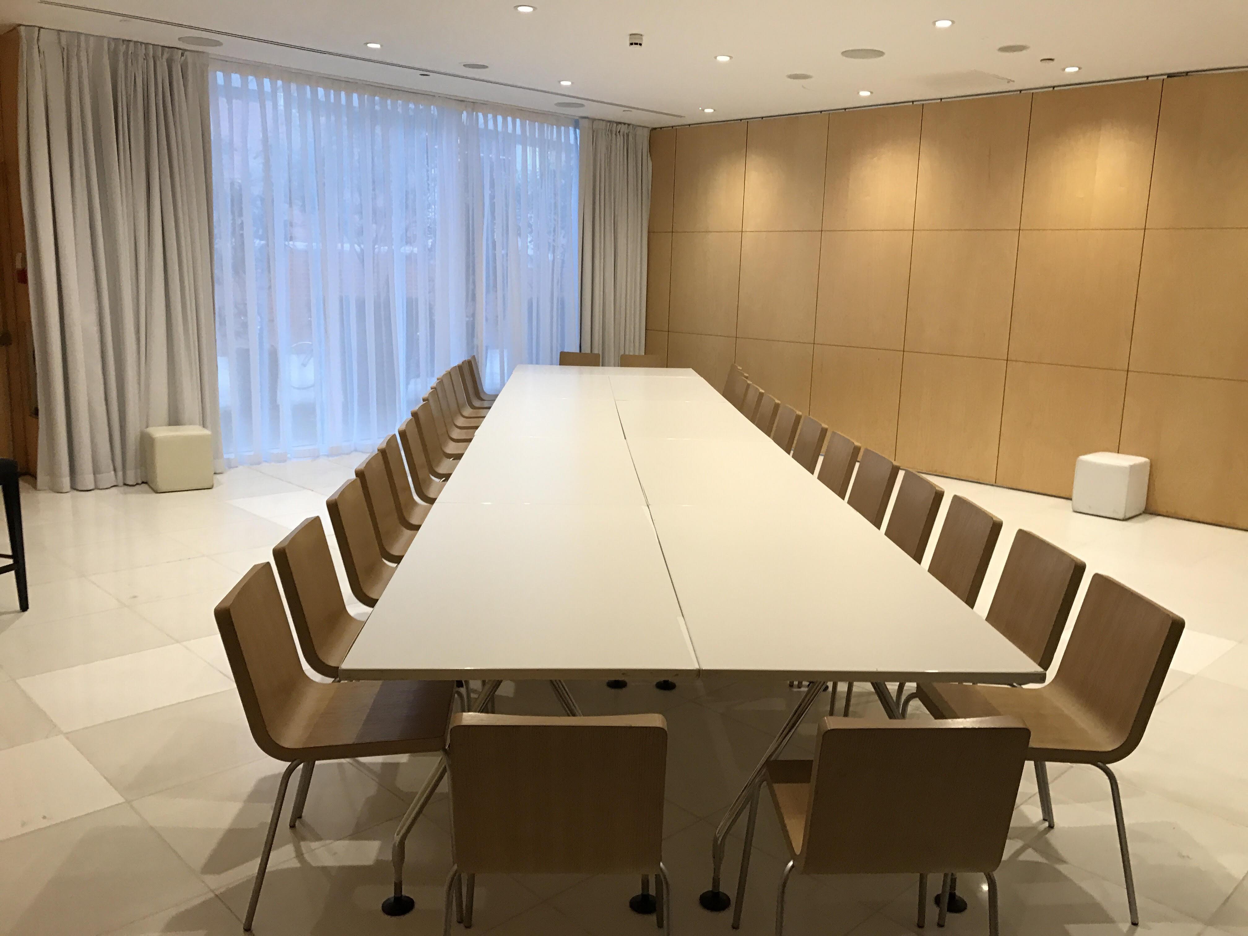 Hotel St Martins Lane Londra Esterno foto The photo shows a spacious meeting room with a long, white table surrounded by wooden chairs. The room features large windows with light-colored curtains, allowing natural light to enter. The walls are made of light wood panels, creating a warm and m