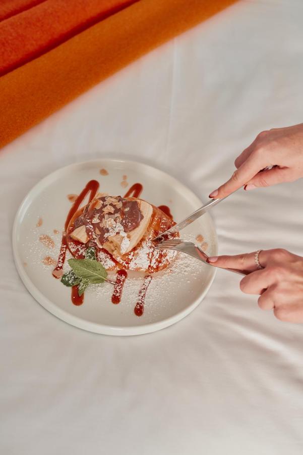 Hotel St Martins Lane Londra Esterno foto The photo depicts a dessert served on a white plate. A person is using a fork and knife to cut into a piece of the dessert, which appears to be a layered cake or pastry topped with chocolate and perhaps caramel sauce. The dessert is garnished with po