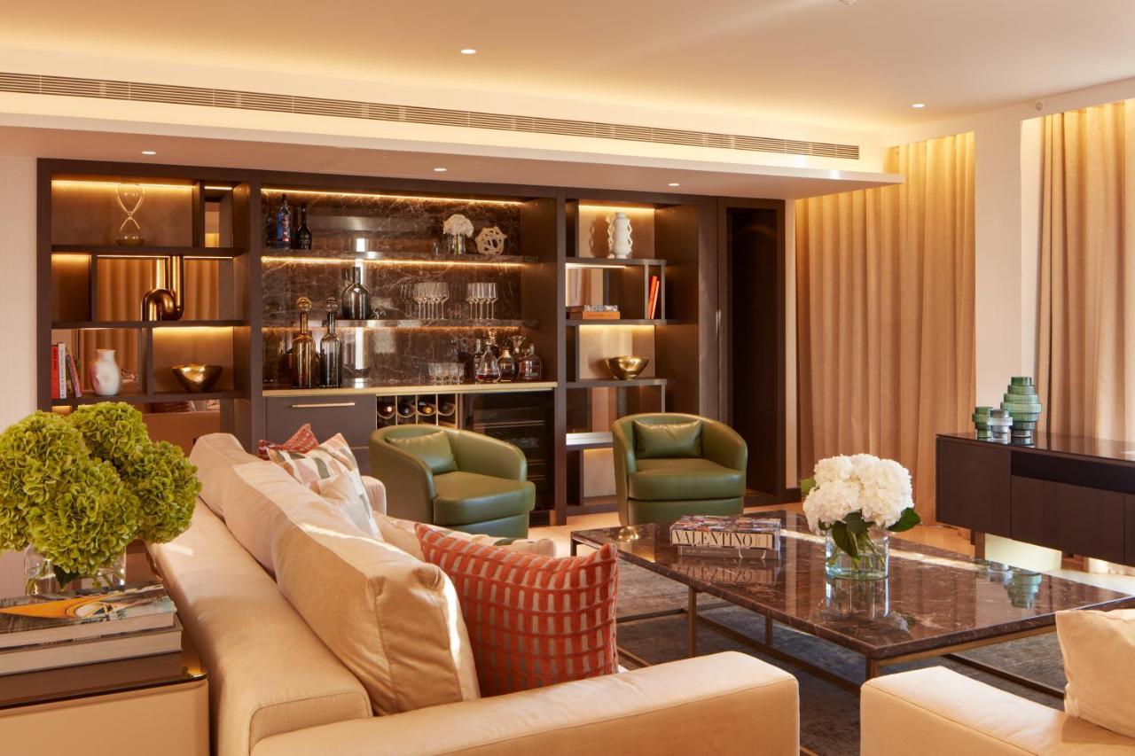 Hotel St Martins Lane Londra Esterno foto The photo depicts a modern and elegantly designed living room. It features a light-colored sofa with decorative cushions, positioning it as a central seating area. Two green armchairs are placed beside a glass coffee table, which sits atop a textured