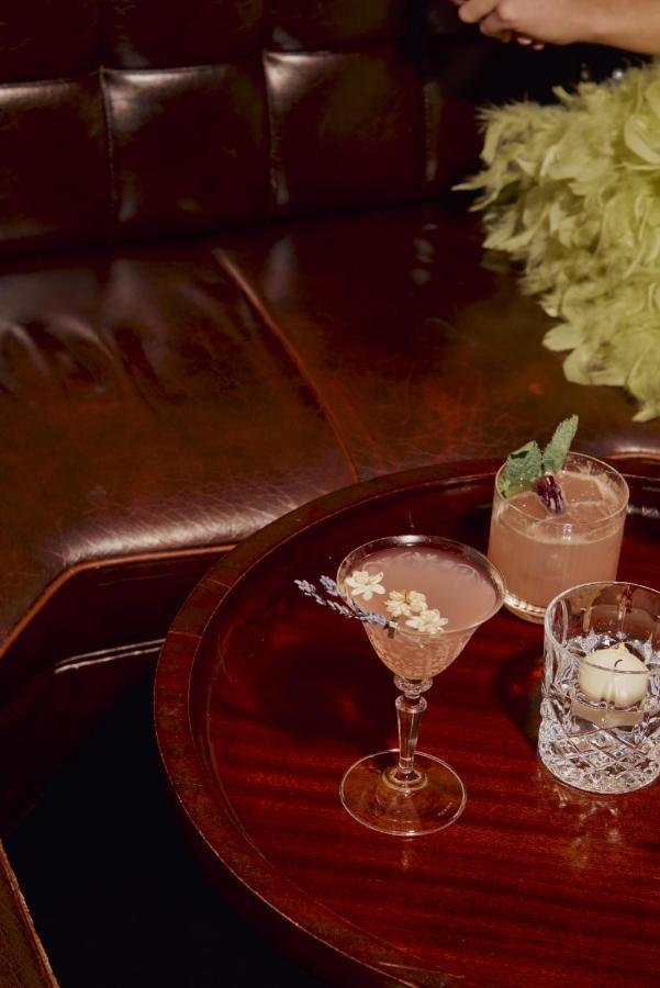 Hotel St Martins Lane Londra Esterno foto The photo shows a cozy setting featuring two cocktails on a wooden table. One drink is in a classic martini glass, garnished with small white flowers. The other is in a short glass with a garnish of mint and some berries. In the background, there is 