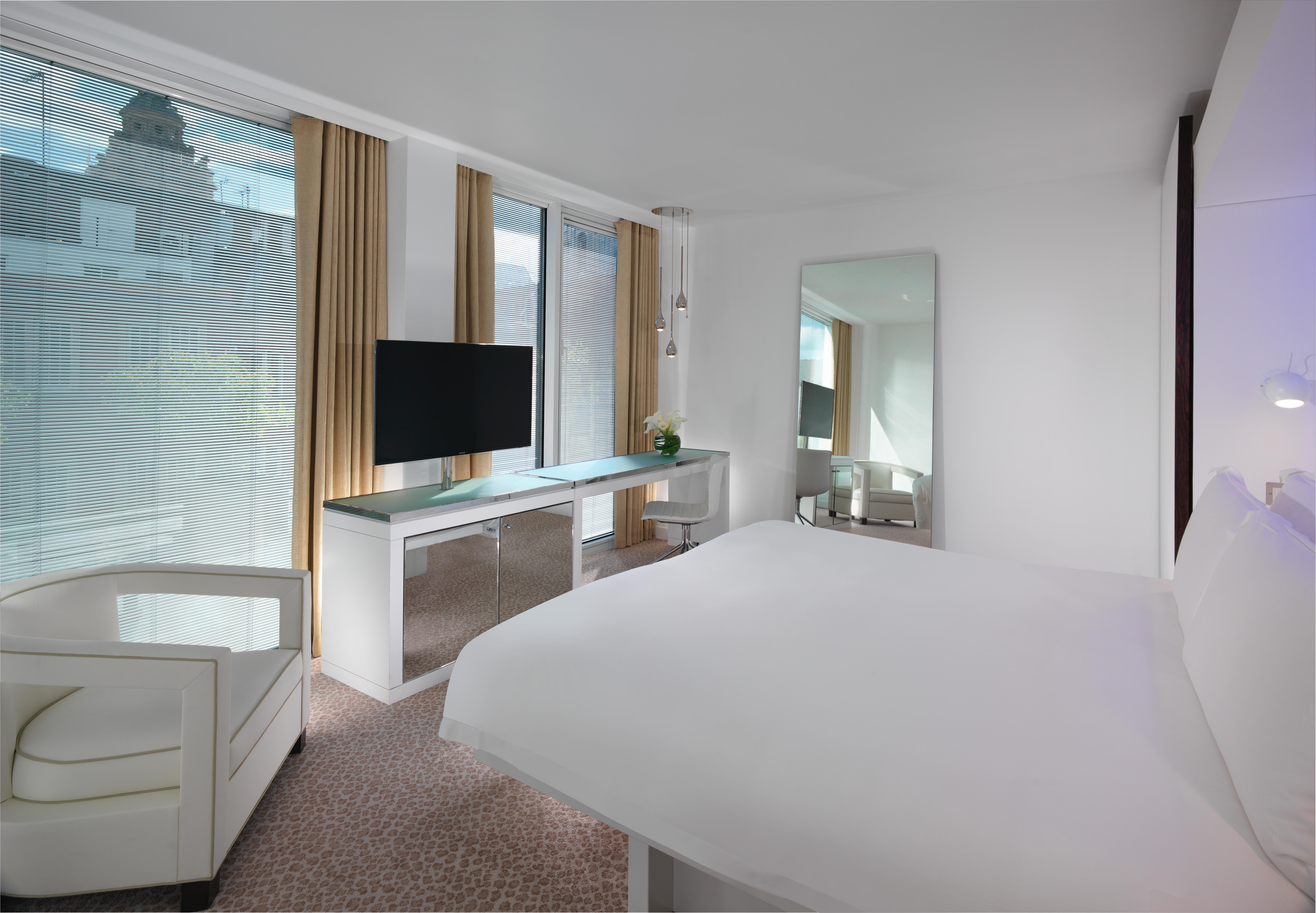 Hotel St Martins Lane Londra Esterno foto The photo shows a modern hotel room featuring a king-sized bed with white bedding. There is a sleek, minimalist design with light-colored walls and a carpeted floor. A large window allows natural light to fill the room, with sheer curtains providing 