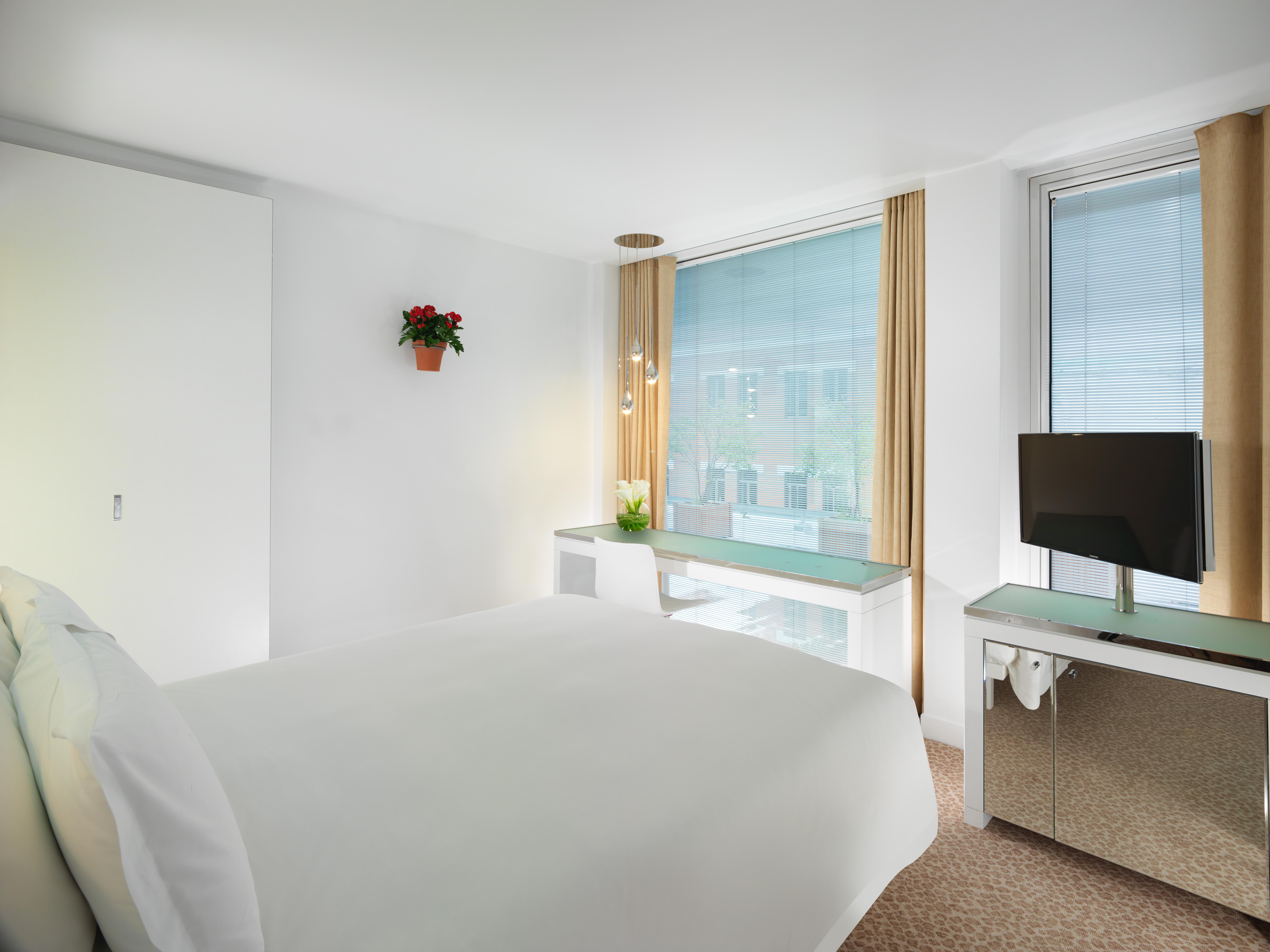 Hotel St Martins Lane Londra Esterno foto The photo shows a bright and modern hotel room. It features a large bed with crisp white bedding, positioned against a clean, light-colored wall. There are two windows with light curtains that allow natural light to enter the space. A small potted pl