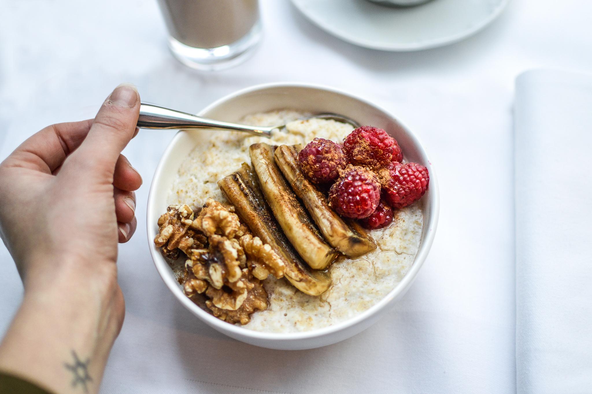 Hotel St Martins Lane Londra Esterno foto The photo shows a bowl of oatmeal topped with sliced bananas, raspberries, and walnuts. A hand holding a spoon is reaching towards the bowl. In the background, there's a glass of a beverage and a plate, suggesting a breakfast setting. The overall pre