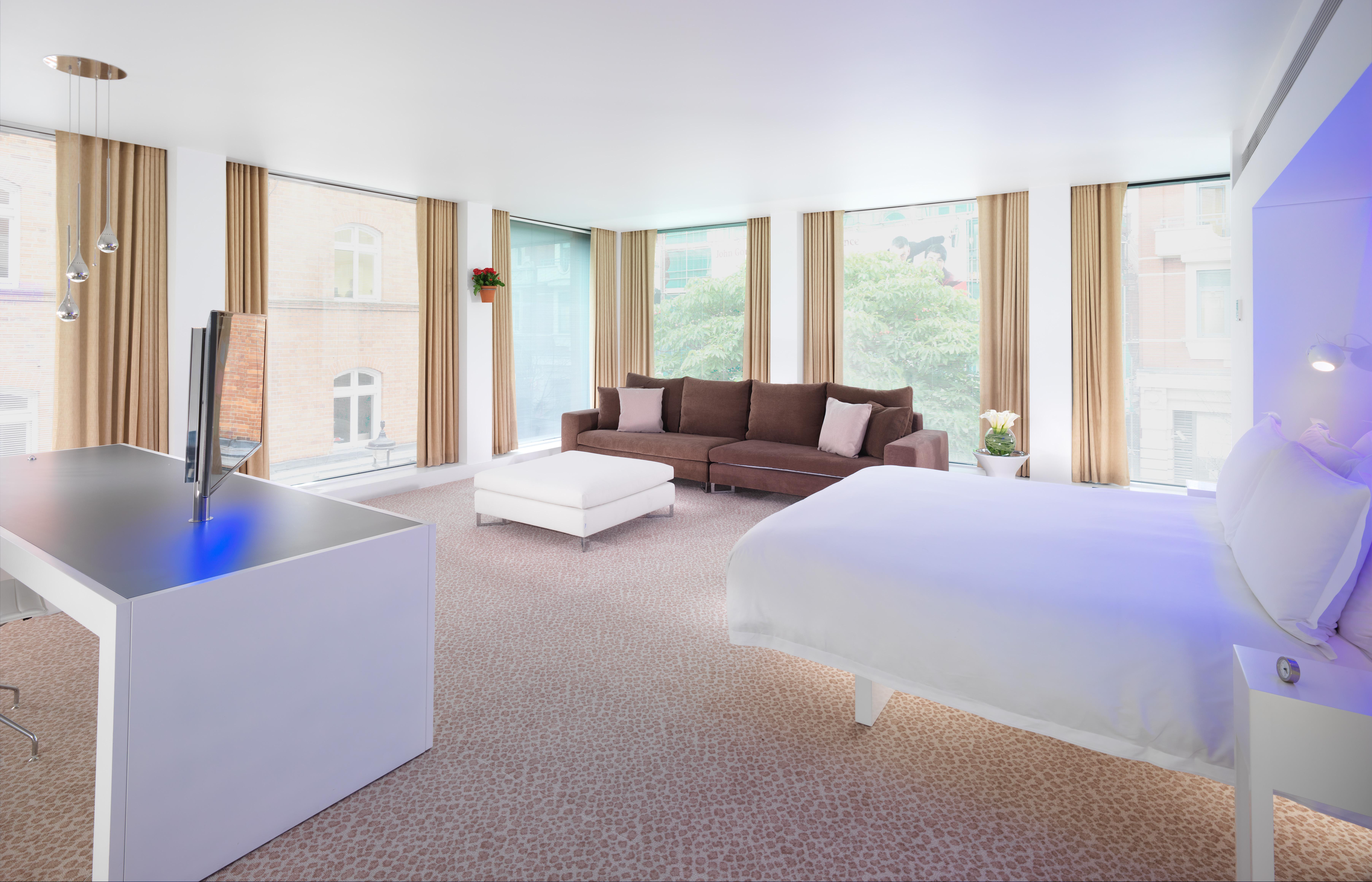 Hotel St Martins Lane Londra Esterno foto The photo shows a modern hotel room with a spacious and bright interior. On one side, there is a large bed with a white comforter. To the other side, there is a cozy brown sofa with some decorative cushions. A white coffee table is placed in front of