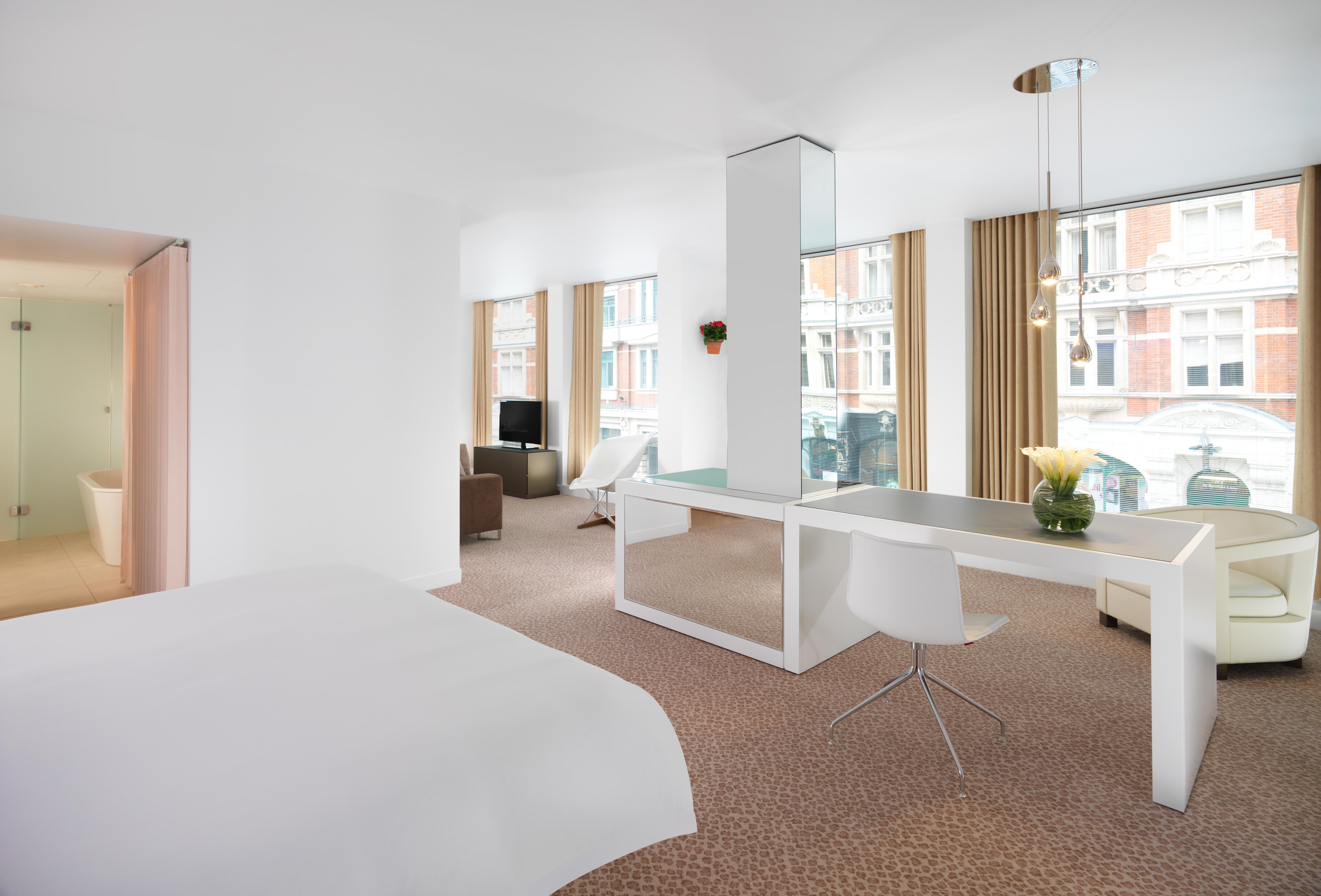 Hotel St Martins Lane Londra Camera foto The photo shows a modern hotel room with a bright, minimalist design. The room features large windows that allow natural light to fill the space. There is a bed with a white duvet in the foreground, and in the background, you can see a workstation wi