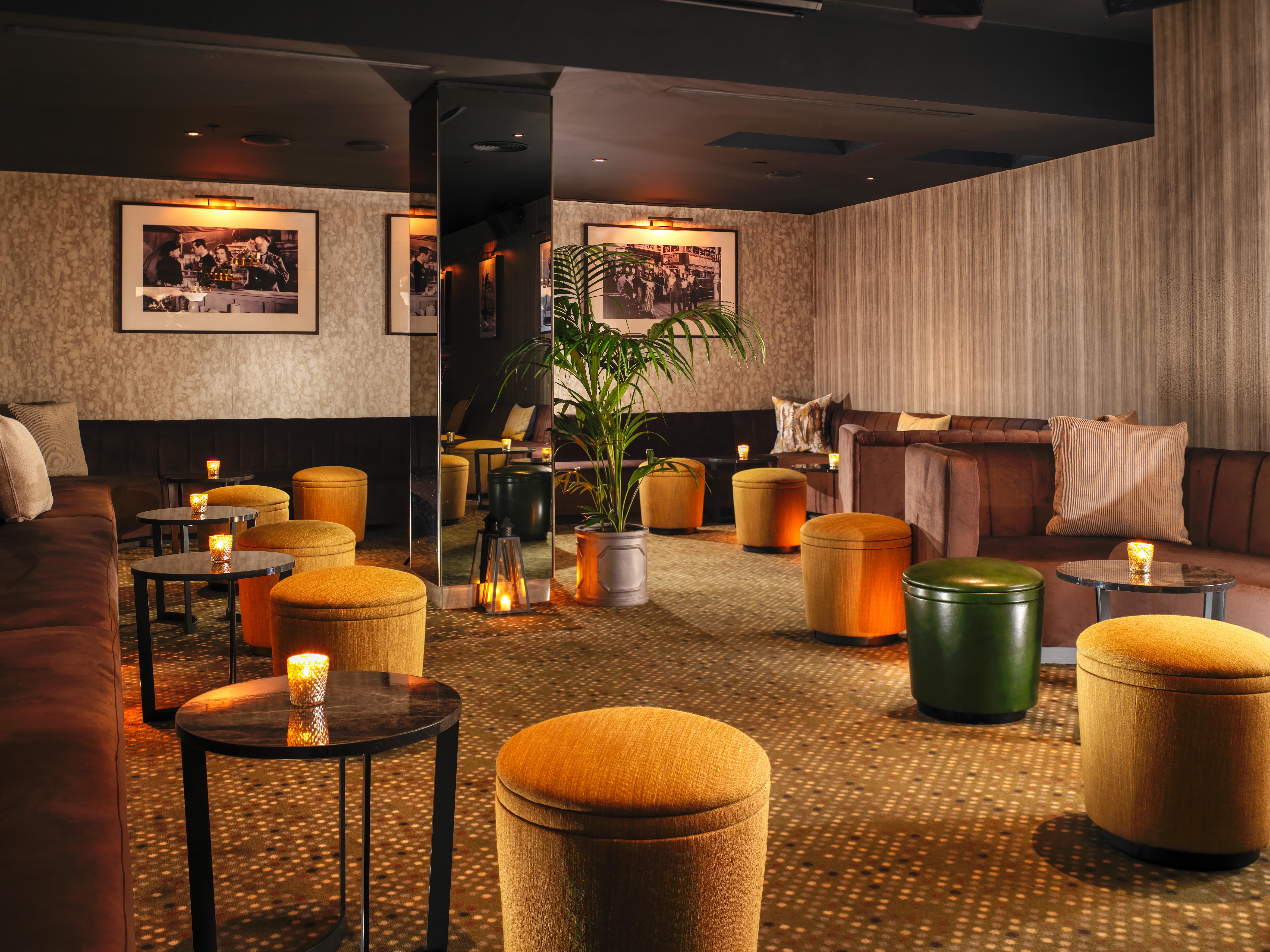 Hotel St Martins Lane Londra Esterno foto The photo shows a cozy lounge area with a warm and inviting atmosphere. The space features a mix of seating arrangements, including cushioned benches and small round tables. There are several colorful ottomans, predominantly in shades of yellow and g