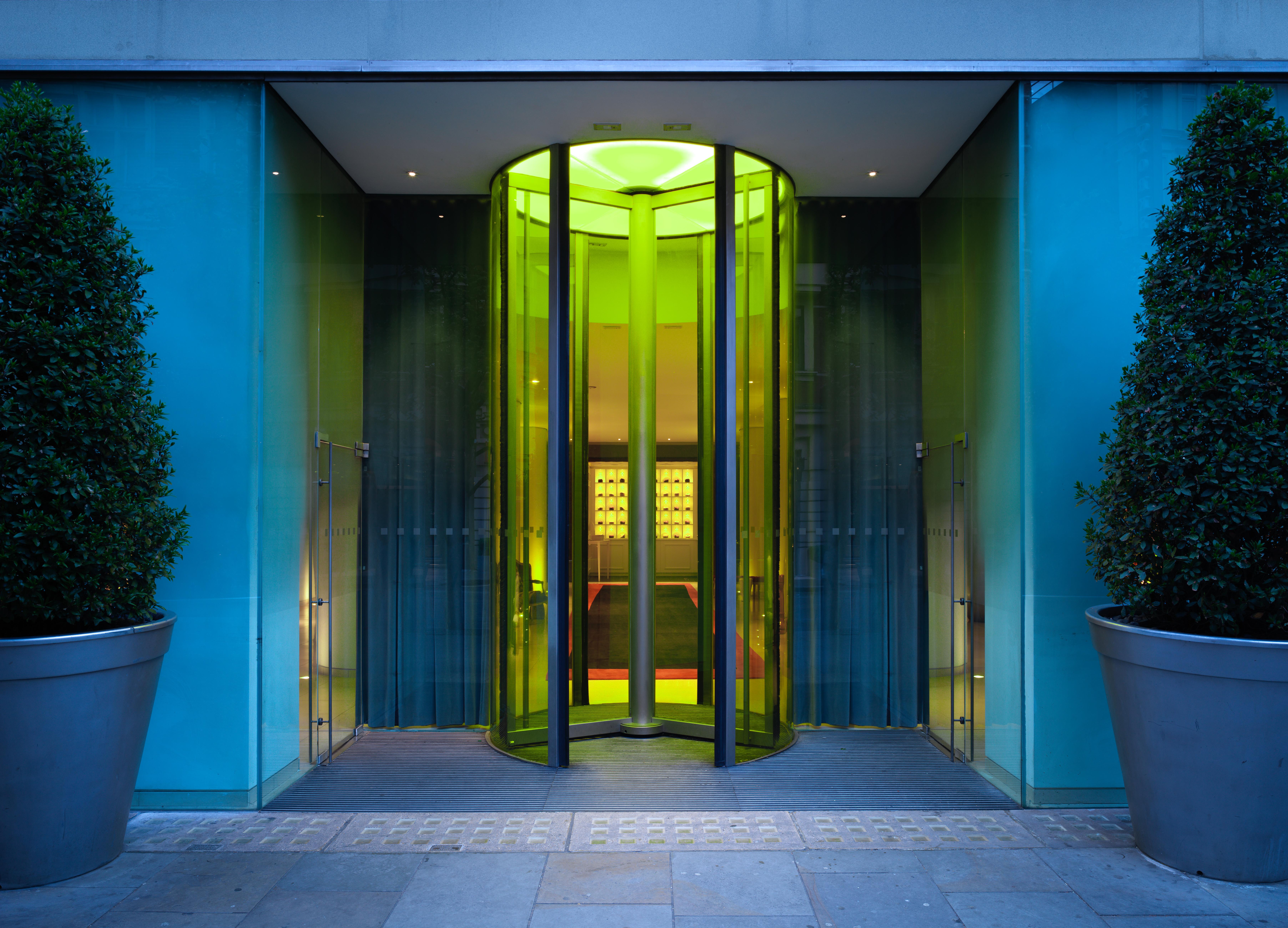 Hotel St Martins Lane Londra Esterno foto The photo shows a modern glass entrance with a revolving door. The door is surrounded by sleek glass panels that reflect light, creating a vibrant ambiance. The entrance is complemented by large, symmetrical planters containing rounded shrubs on eith