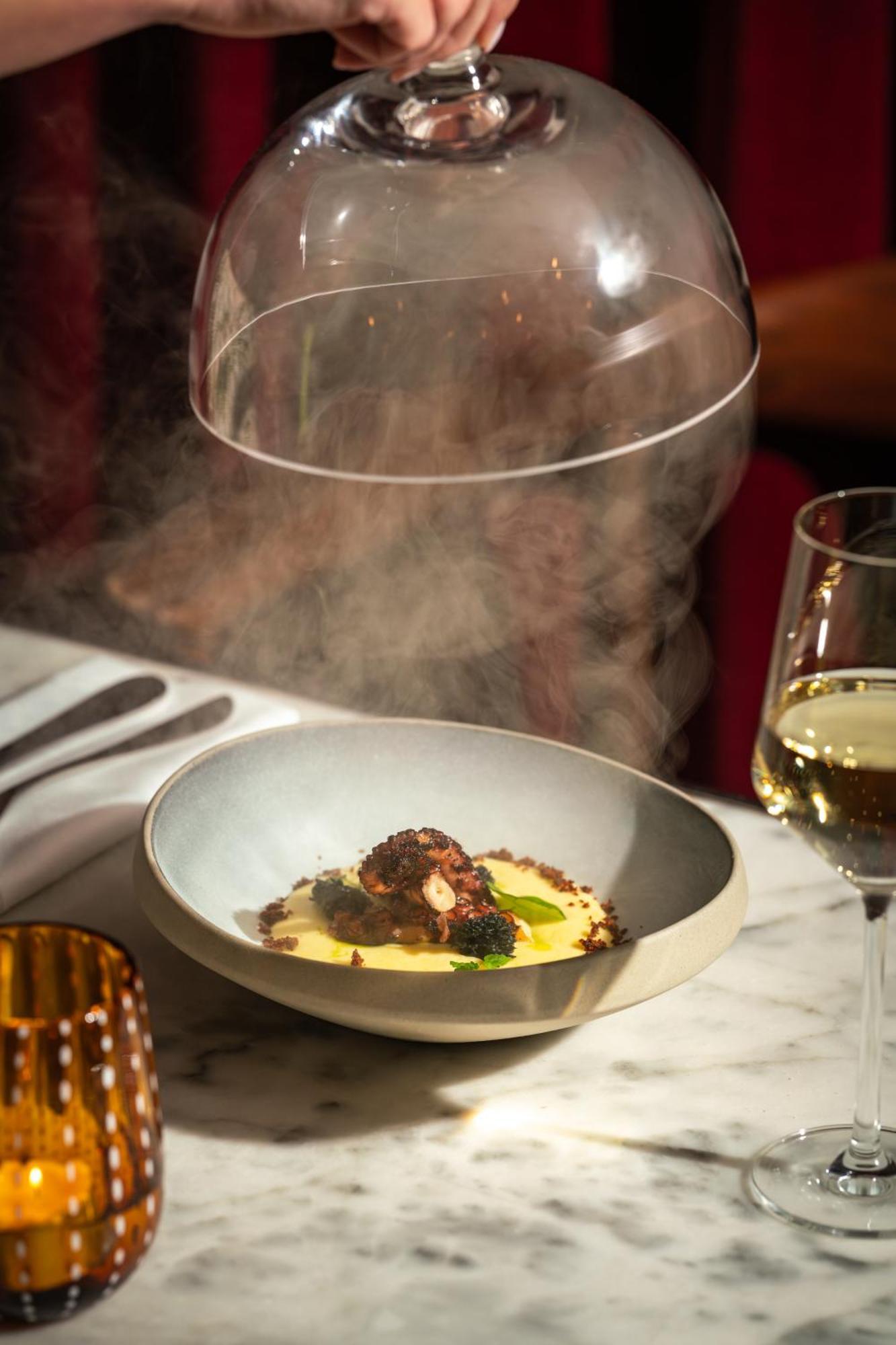 Hotel St Martins Lane Londra Esterno foto The photo depicts an elegant dish served in a shallow bowl. The main feature appears to be octopus, garnished with greens, and placed on a smooth, creamy base, possibly a type of puree. A dome is being lifted from above the dish, releasing steam, whi