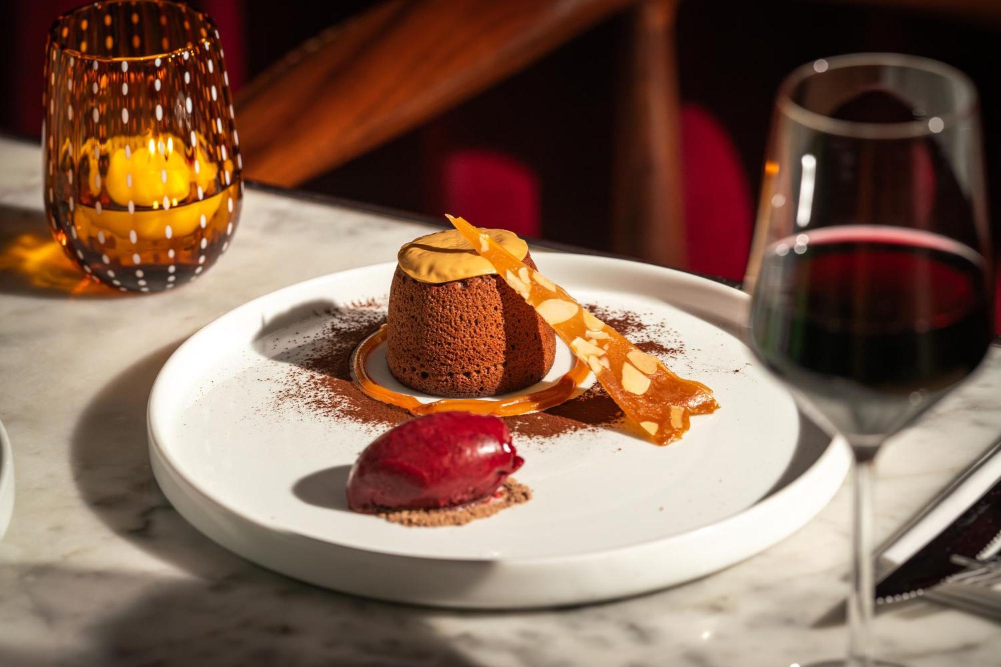 Hotel St Martins Lane Londra Esterno foto The photo showcases an elegantly presented dessert on a white plate. At the center is a chocolate dessert, likely a mousse or soufflé, adorned with a delicate strip of caramel or chocolate. Surrounding it is a sprinkle of cocoa powder. Beside the cho