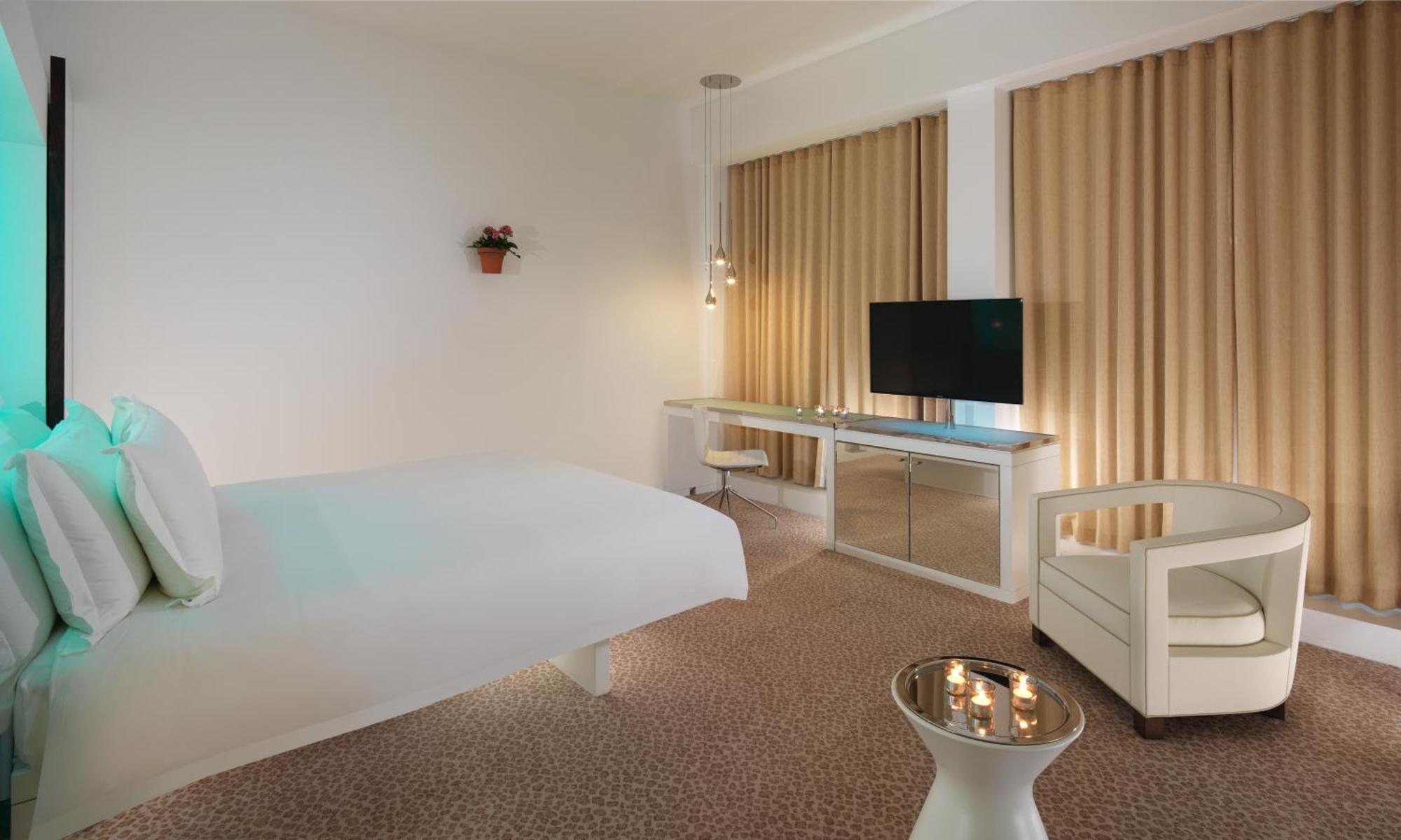Hotel St Martins Lane Londra Esterno foto The photo shows a modern hotel room with a minimalist design. It features a large bed against one wall, a flat-screen TV mounted on another wall, and a contemporary desk with a mirror. Large windows are dressed with light-colored curtains, allowing n