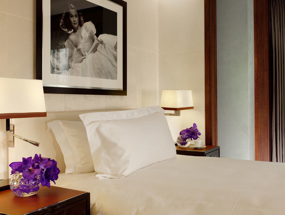 Hotel St Martins Lane Londra Esterno foto The photo shows a stylishly decorated bedroom. It features a neatly made bed with a white bedspread and a large white pillow. On either side of the bed, there are dark wood nightstands with decorative lamps. Each nightstand has a small vase containin